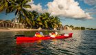 A red tandem sea kayak with two people in it paddling along the beach lines with palm trees on a sunny evening in Cuba