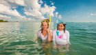 Two women standing up in the Caribbean with their snorkels on their head smiling